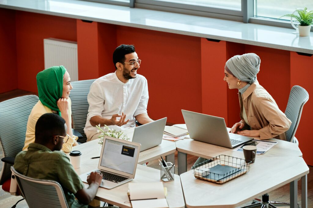 A group of diverse coworkers engaging in a collaborative discussion with laptops in a modern office setting.